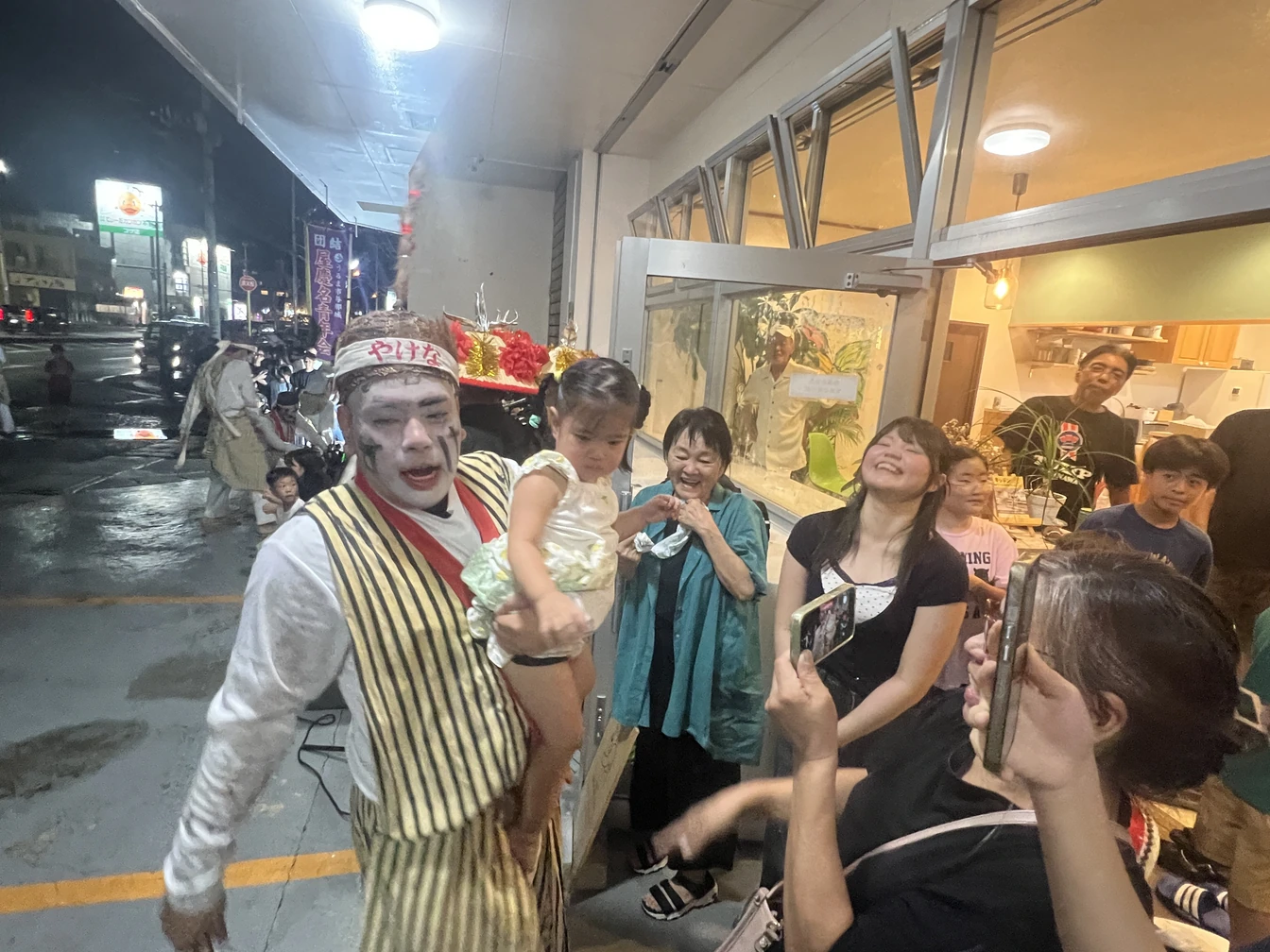 お子さまを抱く屋慶名青年会の方と、周りで笑顔を見せる来場者