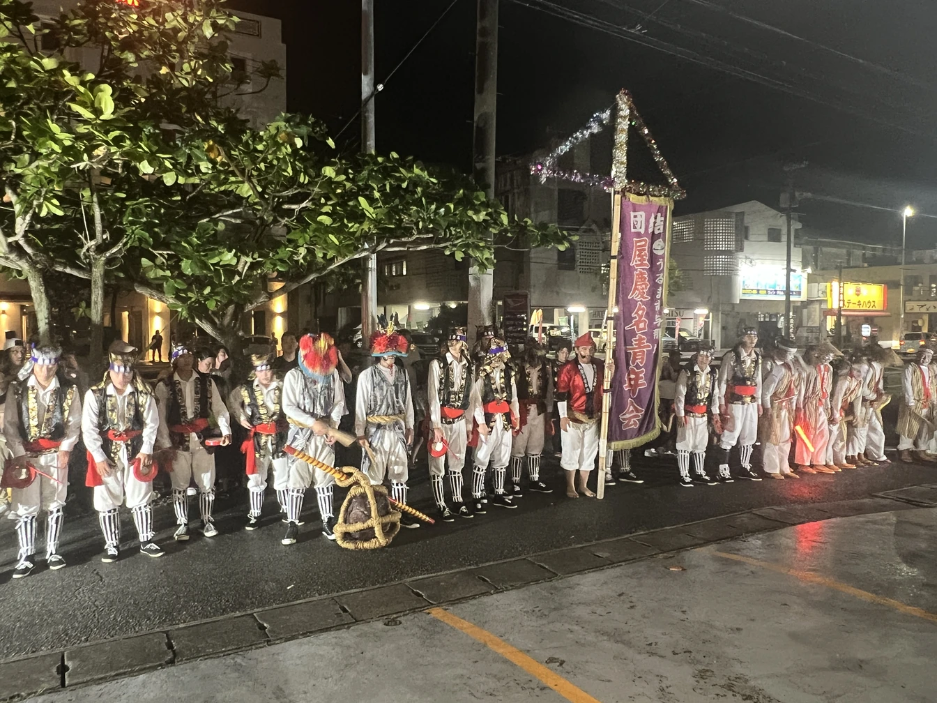 屋慶名青年会の旗のもとに、衣装姿で並ぶ皆さま